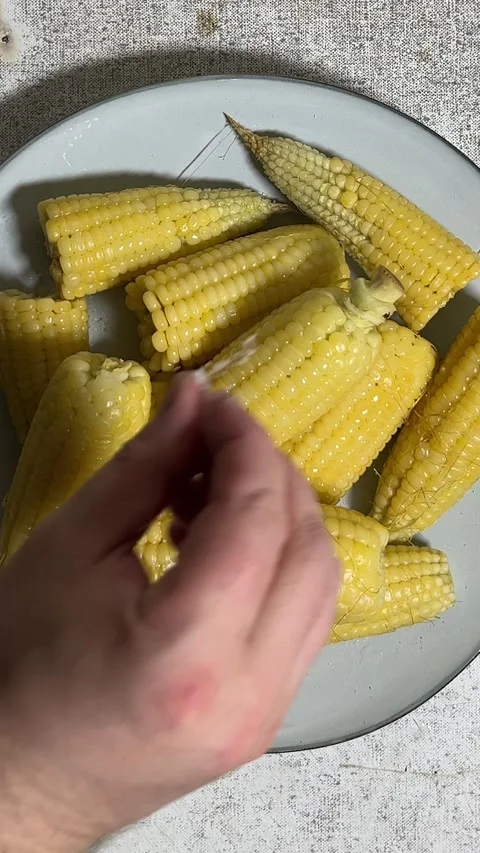 Cooking process. Man sprinkles salt on pieces of boiled half an cob of corn Video stock 281795142
