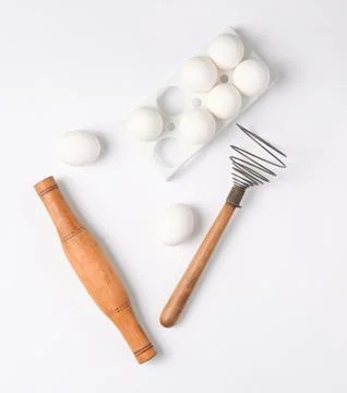 The cooking process. Plastic tray with white eggs, rolling pin, whisk on a wh Stock Photos