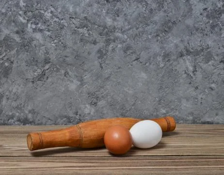 The cooking process. Rolling pin, eggs on a wooden shelf on a concrete wall Stock Photos