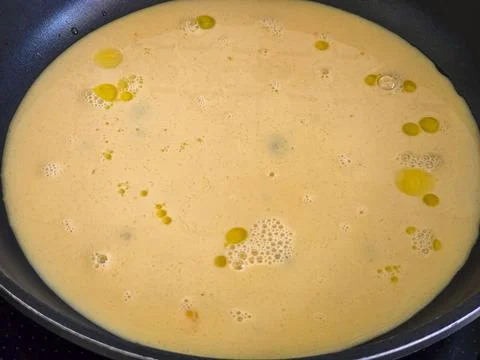 Cooking raw egg mixture with olive oil droplets in a non stick pan for brea.. Foto stock