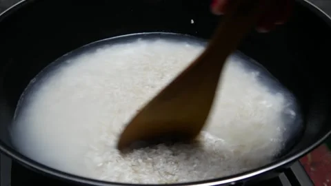 Cooking rice in a black pan, stirring using a wooden spatula Stock Footage 304721833