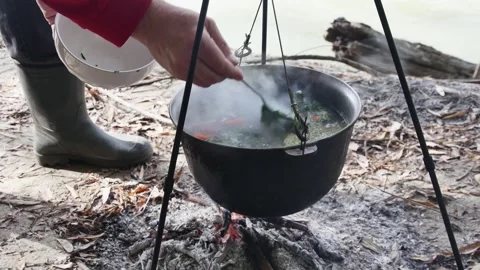 Cooking river fish soup in a cauldron on a fire on the river bank, the fishe Видео 254062233