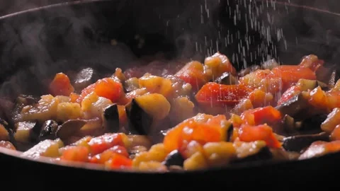 Cooking roasted vegetables. Chef adds salt to steaming hot pan. Stock Footage 250595591