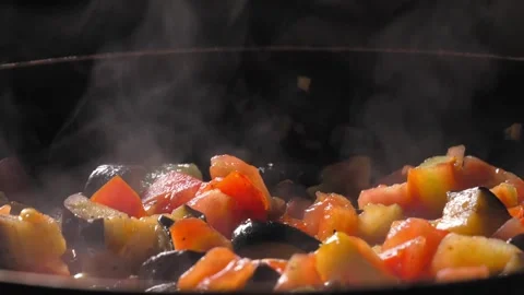 Cooking roasted vegetables. Chef stirs with spoon into steaming hot pan Stock Footage 250777097