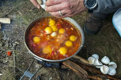 Cooking scrambled eggs with vegetables on the fire in the woods Stock Photos