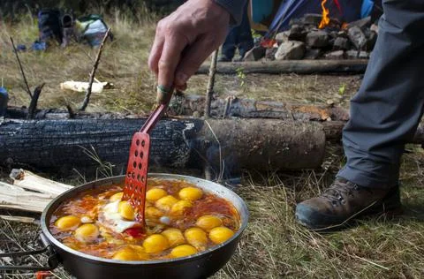 Cooking scrambled eggs with vegetables on the fire in the woods Stock Photos