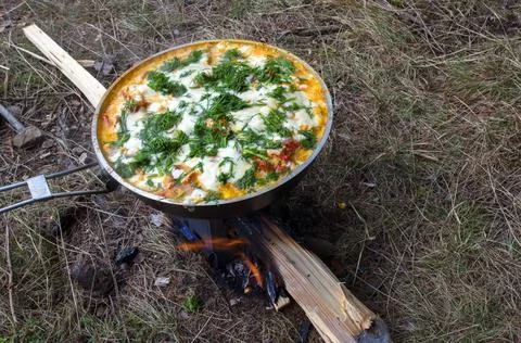 Cooking scrambled eggs with vegetables on the fire in the woods Stock Photos