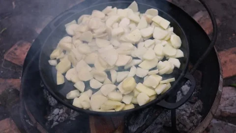Cooking sliced potatoes in a cast iron skillet over an open fire Stock Footage 337105643