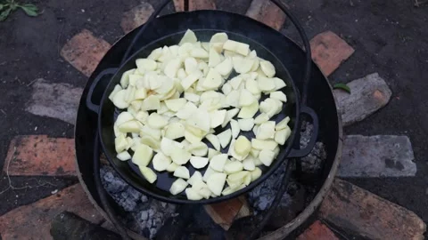 Cooking sliced potatoes in a large cast iron skillet over an open fire Stock Footage 337105592
