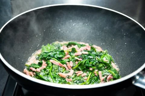 Cooking spinach with diced bacon Stock Photos