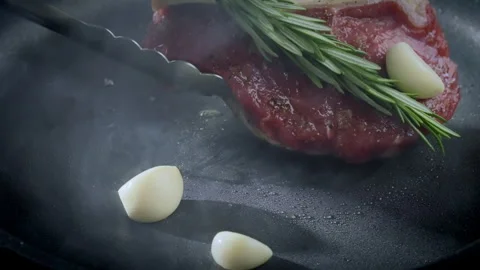 Cooking the steak. The chef cooks a steak in a pan with garlic and rosemary. Video stock 263346032