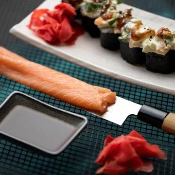 Cooking sushi. Thin slice of red salmon fish or sturgeon fillet on kitchen knife Stock Photos