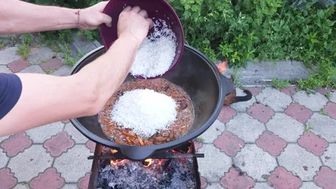 Cooking Uzbek pilaf. Adding Laser rice to boiling zirvak Stock Footage 244484677