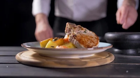 Cooks hand puts a fresh fried steak on white plate and maiking final decoration Stock Footage 127050828