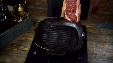 The cook's hand putting a beef steak on the hot broiler pan for frying. 4K Stock Footage 84205990