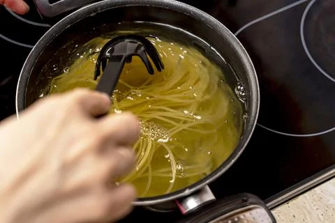 Cook's hand stirs spaghetti cooked in a saucepan with a slotted spoon Foto stock