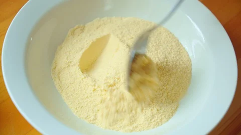 Cook's hand stirs yellow corn flour in white bowl by spoon on wooden table. Stock Footage 127779427