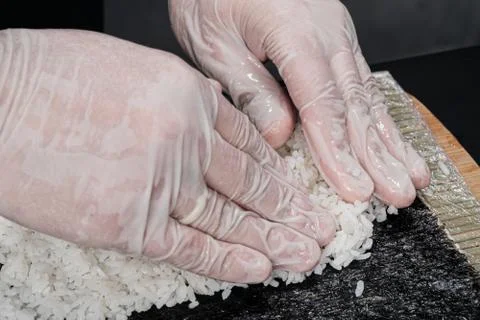 Cook's hands close-up. The chef makes sushi and rolls from rice. White gloves. Stock Photos