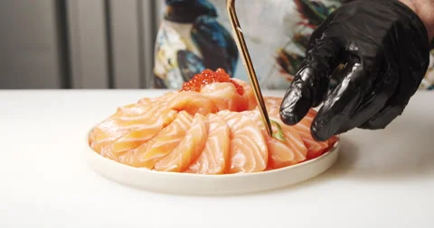 Cook's hands decorating greens a dish of slices of salmon and red caviar Stock Footage 134282372