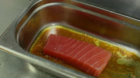 The cook's hands flipping a piece of raw tuna in a bowl of marinade.close-up Stock Footage 115659484