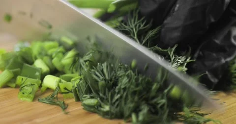 Cook's hands in gloves are chopping greenery dill and onion on wooden board. Stock Footage 147347228