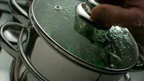 Cook's hands opens the lid of the pan and shows green broccoli steamed Stock Footage 113605803