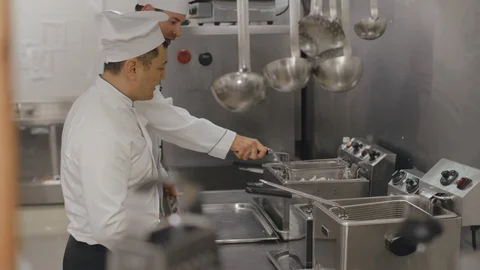 Cooks in uniform using fryer while cooking in restaurant kitchen Stock Footage 125050671