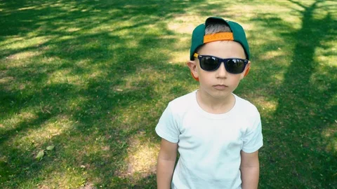 A cool 5 year old boy in sunglasses stands in the summer park and starts smiling Stock Footage 89697487