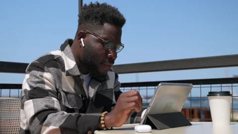 Cool african american guy is using tablet with in-ear headphones, resting in Stock Footage 231901395