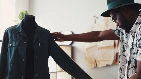Cool Afro-American tailor takes measures on mannequin, writes them down in his Stock Footage 87030255