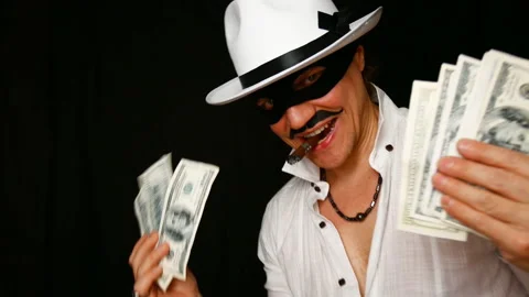 Cool bad guy with a black mask, white hat, cigar and money on a black backdrop Video stock 141855810