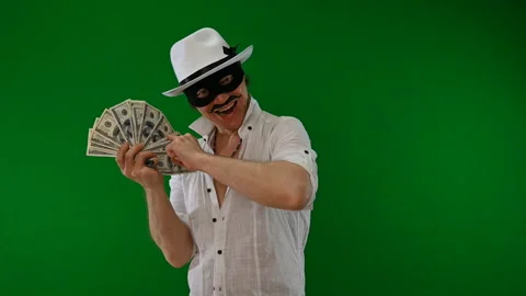 Cool bad guy with a black mask, white hat, cigar and money on a green backdrop Stock Footage 141856003