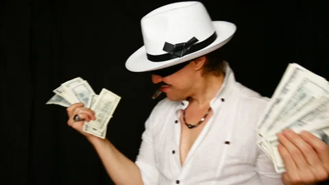 Cool bad guy with a black mask, white hat, cigar and money on a black backdrop Stock Footage 141856062
