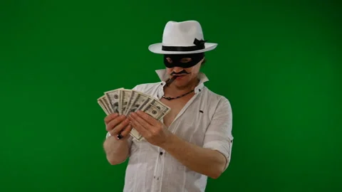 Cool bad guy with a black mask, white hat, cigar and money on a green backdrop Stock Footage 141856158