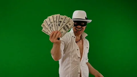 Cool bad guy with a black mask, white hat, cigar and money on a green backdrop Stock Footage 141856383