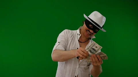 Cool bad guy with a black mask, white hat, cigar and money on a green backdrop Stock Footage 141856384