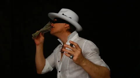 Cool bad guy with a black mask, white hat, cigar and money on a black backdrop Video stock 142540992