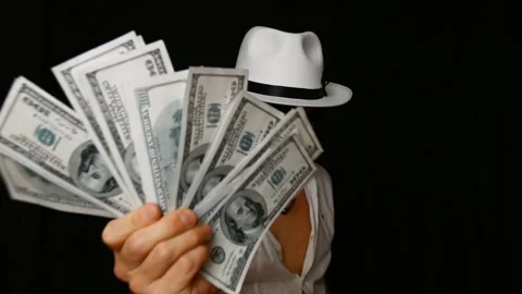 Cool bad guy with a black mask, white hat, cigar and money on a black backdrop 스톡 동영상 142541150