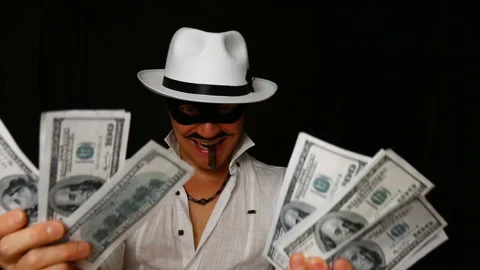 Cool bad guy with a black mask, white hat, cigar and money on a black backdrop Stock Footage 142541176