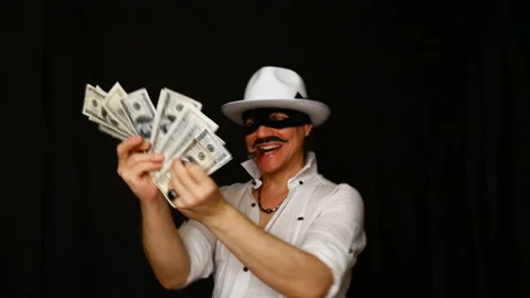 Cool bad guy with a black mask, white hat, cigar and money on a black backdrop Video stock 142541178