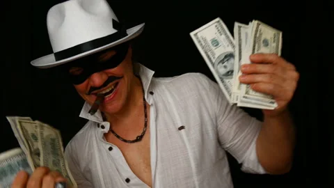 Cool bad guy with a black mask, white hat, cigar and money on a black backdrop Stock Footage 142541994