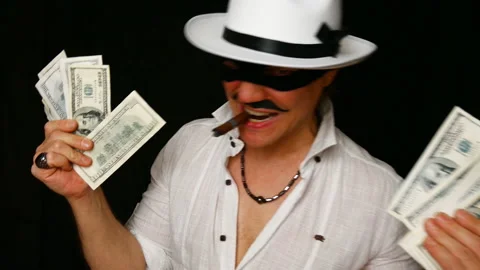Cool bad guy with a black mask, white hat, cigar and money on a black backdrop Stock Footage 142542169