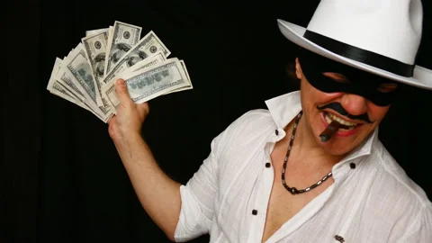 Cool bad guy with a black mask, white hat, cigar and money on a black backdrop Stock Footage 142542670