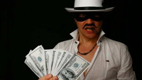 Cool bad guy with a black mask, white hat, cigar and money on a black backdrop Stock Footage 142543076