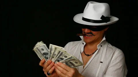 Cool bad guy with a black mask, white hat, cigar and money on a black backdrop Stock Footage 142543200