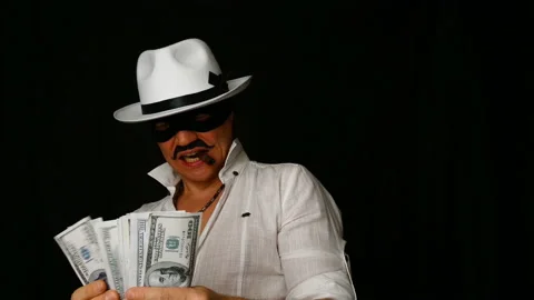Cool bad guy with a black mask, white hat, cigar and money on a black backdrop Stock Footage 142543238