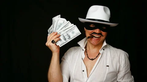 Cool bad guy with a black mask, white hat, cigar and money on a black backdrop Stock Footage 142543389