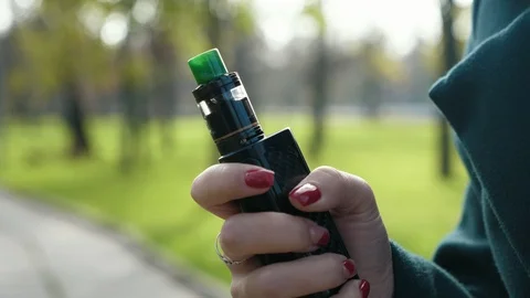 Cool black box mod device for vaping with green drip tip in hand of young girl Stock Footage 119942248