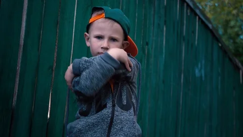 Cool boy changes facial expressions, child posing on camera near old wooden Stock Footage 89130652