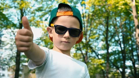 A cool boy in sunglasses shows a class with his finger up standing in a summer Video stock 89696900